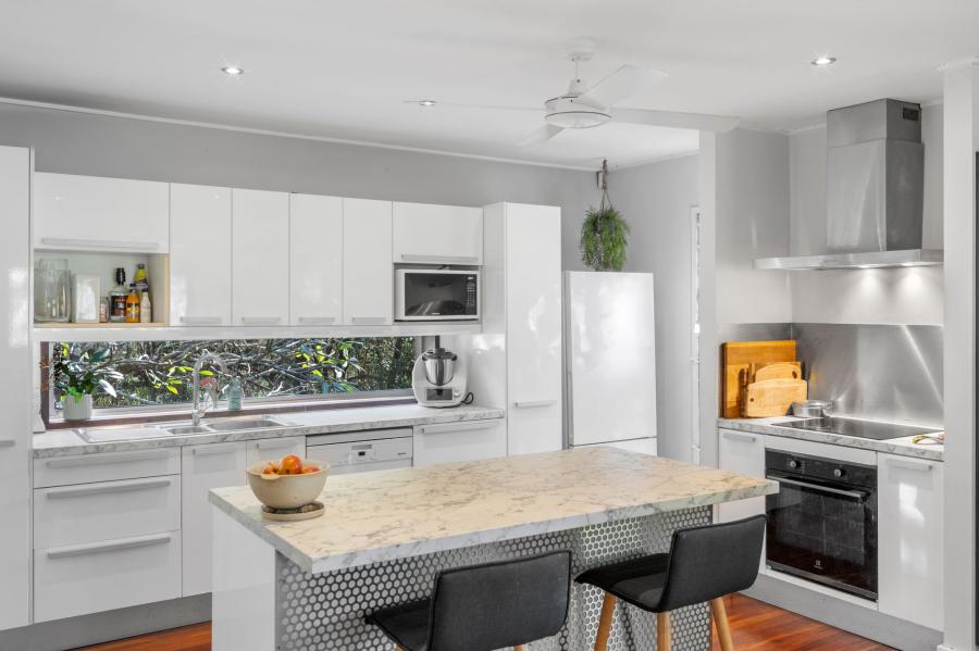 A white kitchen with a marble island and a garden-view splashback