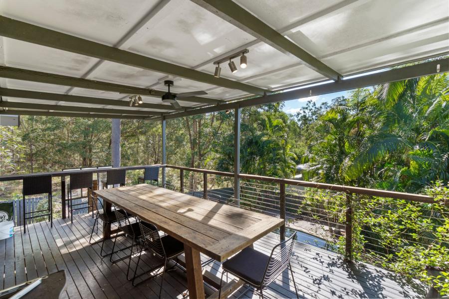 A covered timber deck with a dining table surrounded by bushland